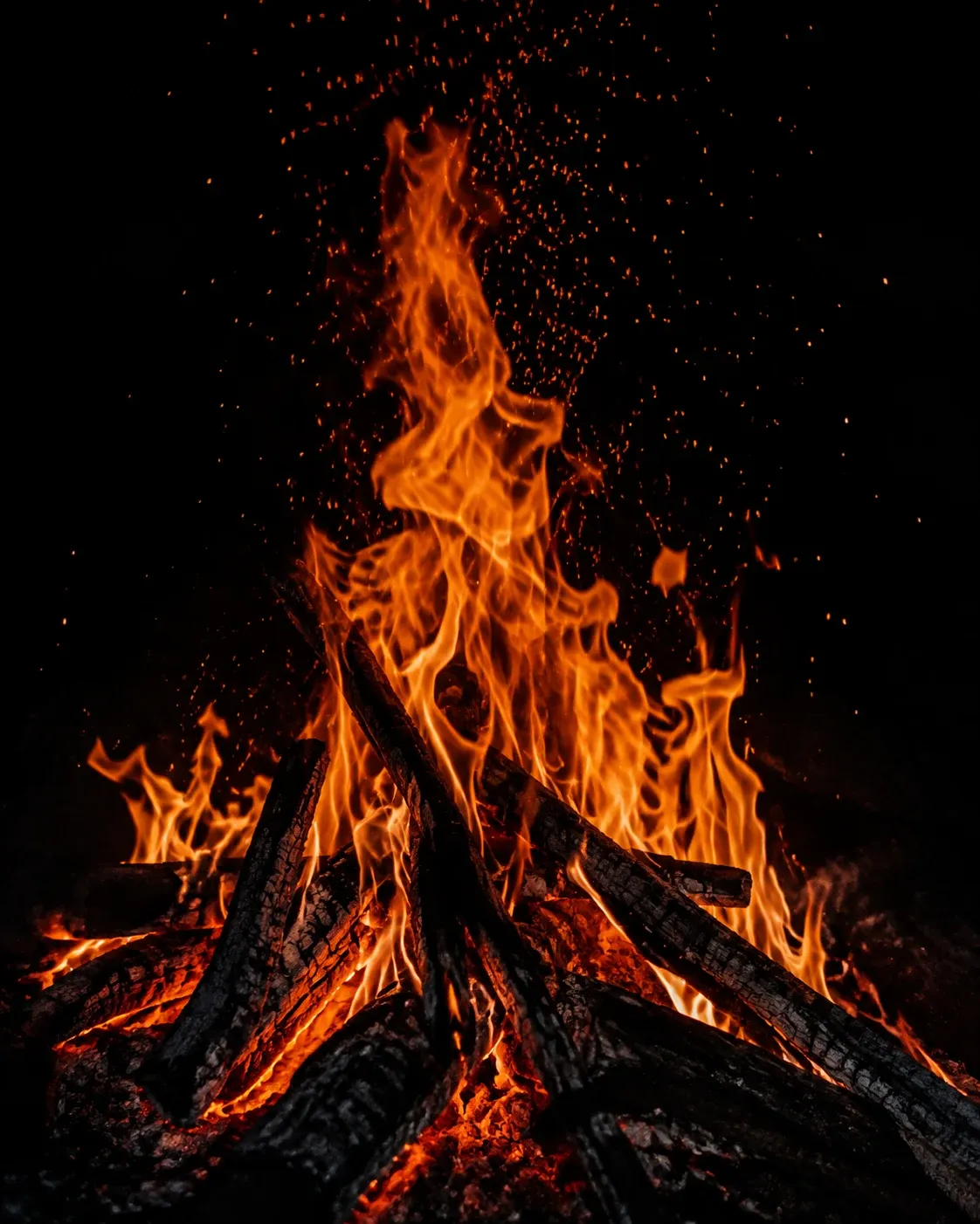 Flames and sparks rising from glowing, charred wood into the night.