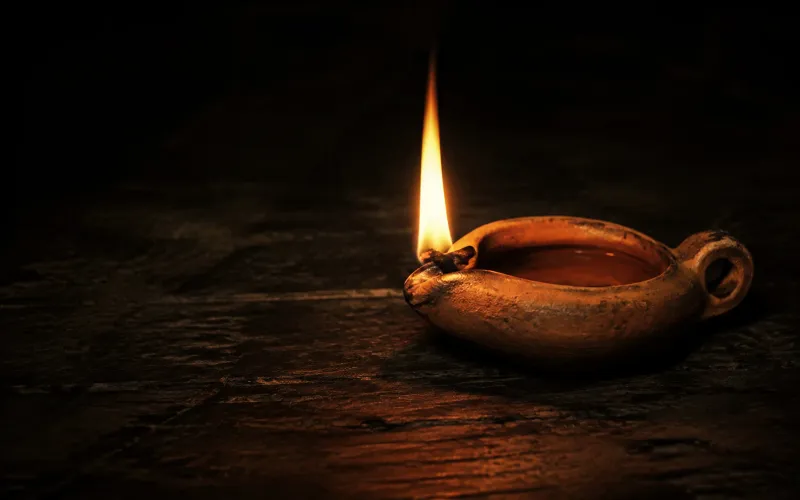 A single flame illuminating an earthenware oil lamp in darkness.