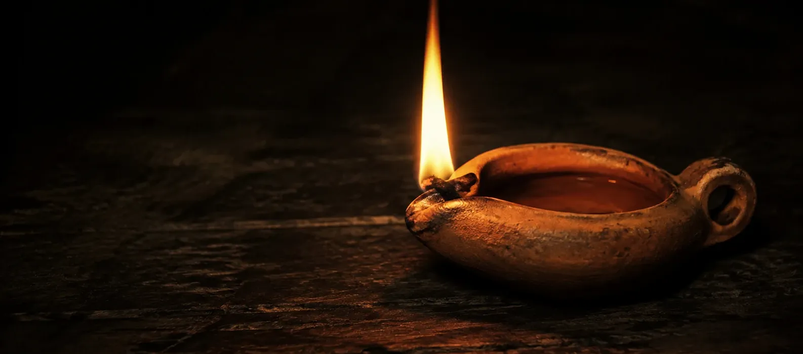 A single flame illuminating an earthenware oil lamp in darkness.